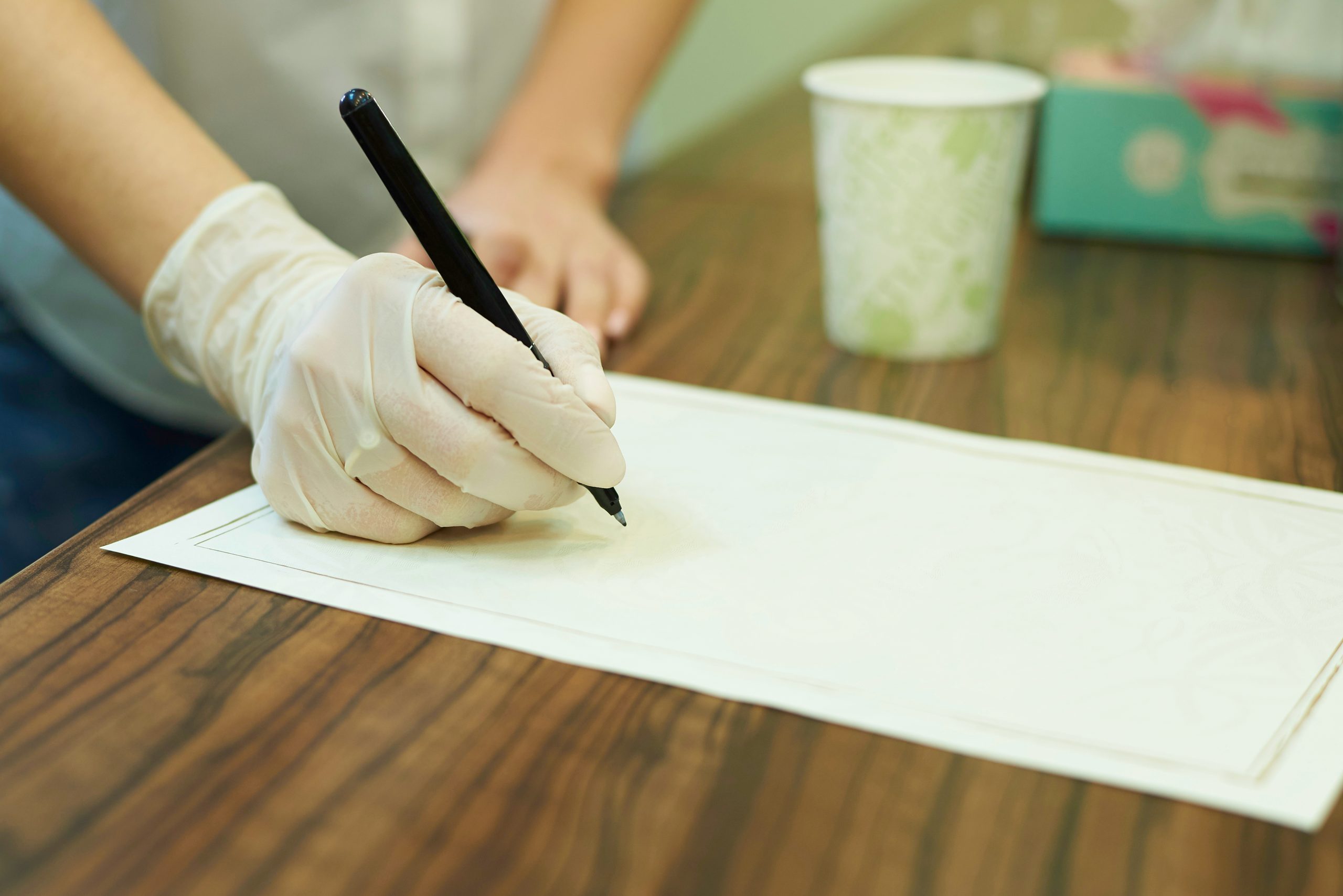 Person's hand with surgical gloves holding pen on blank paper